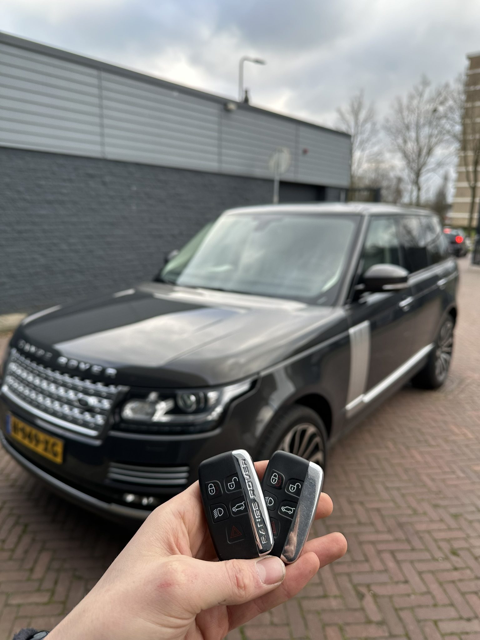 Twee Range Rover-smartkeys in de hand, met de zwarte Range Rover op de achtergrond
