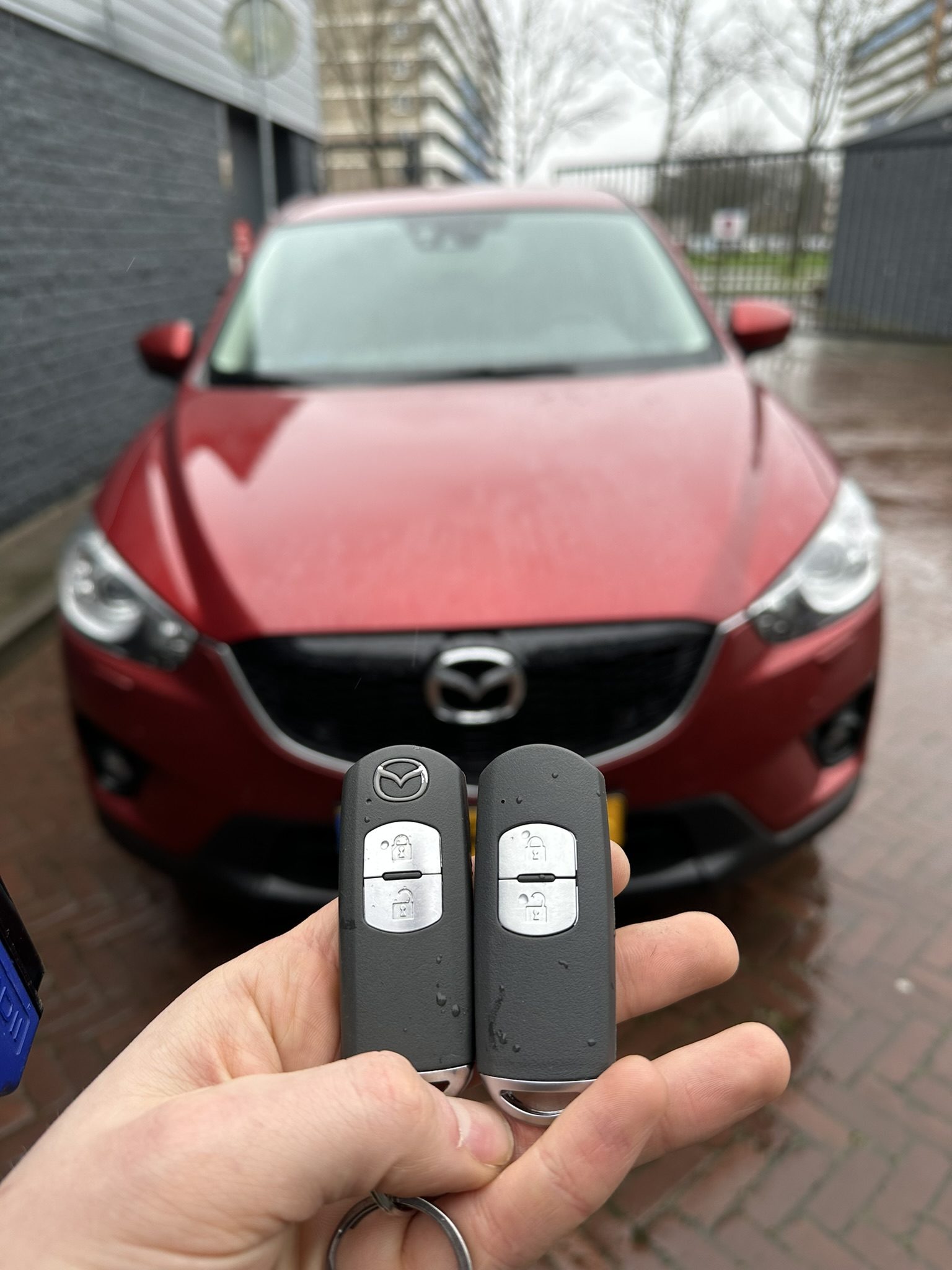 Twee Mazda-smartkeys in de hand, met de rode Mazda CX-5 op de achtergrond