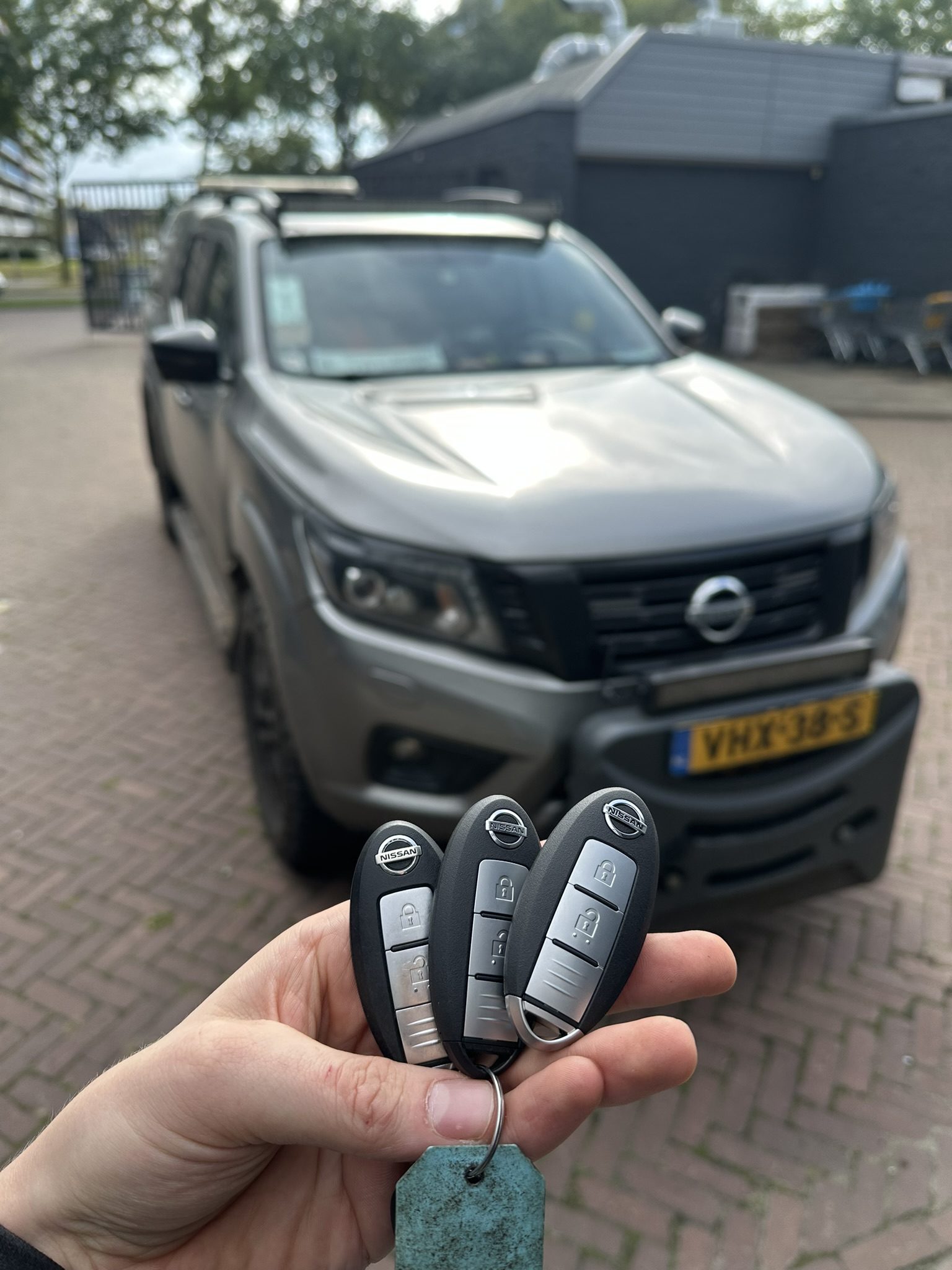 Drie Nissan-sleutels in de hand, met de Nissan Navara op de achtergrond