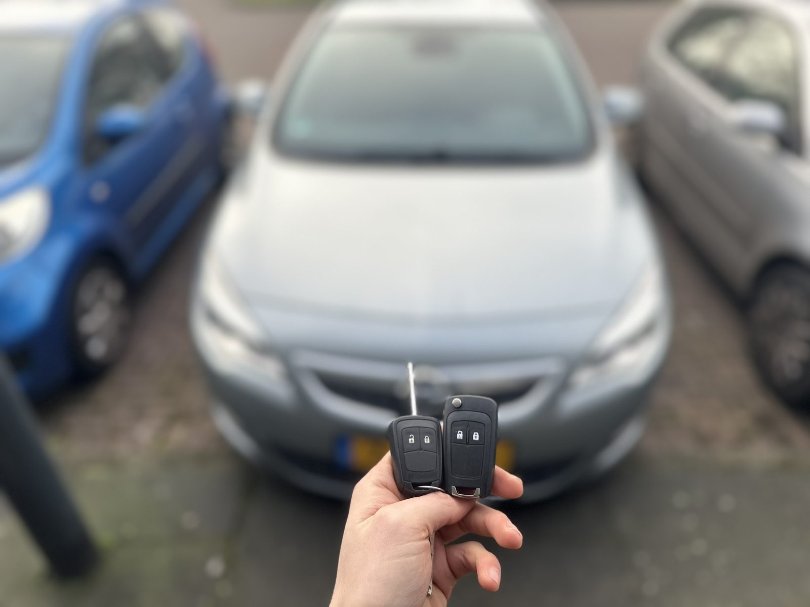 Twee Opel-klapsleutels in de hand, met de Opel Astra op de achtergrond