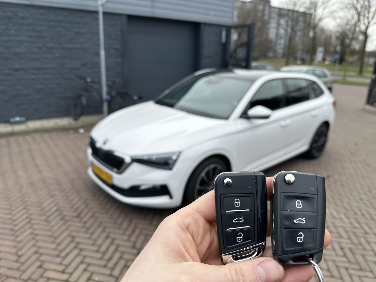Twee Skoda-klapsleutels in de hand, met de witte Skoda op de achtergrond
