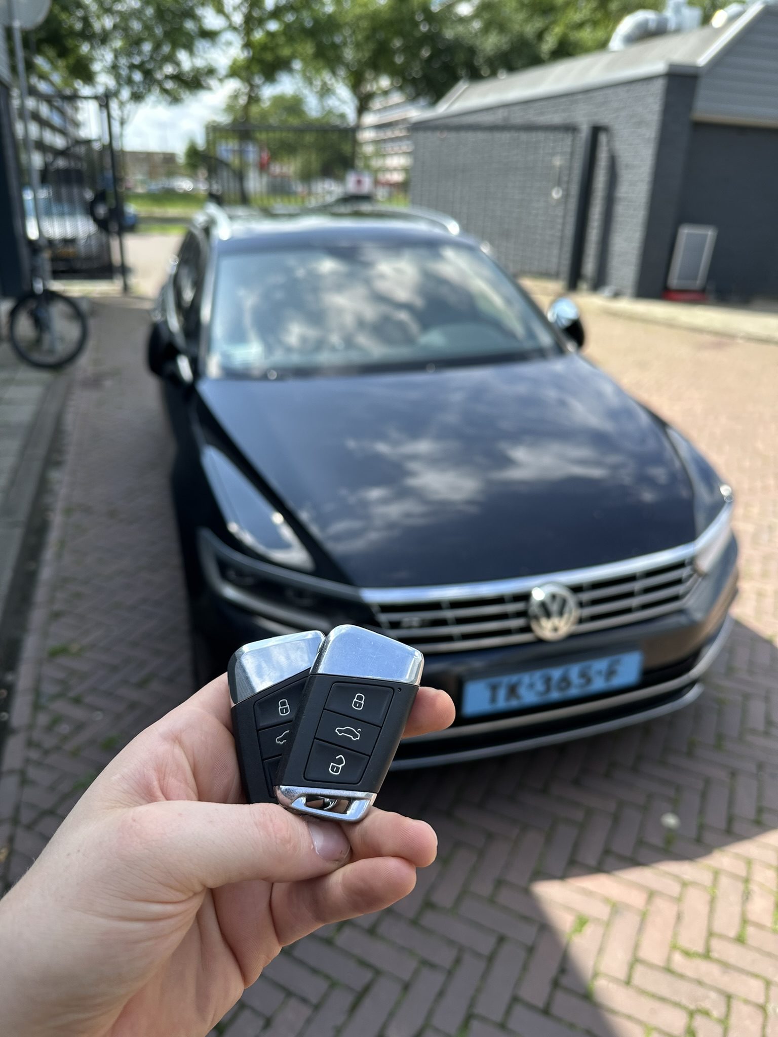 Twee Volkswagen-smartkeys in de hand, met de donkerblauwe Passat op de achtergrond